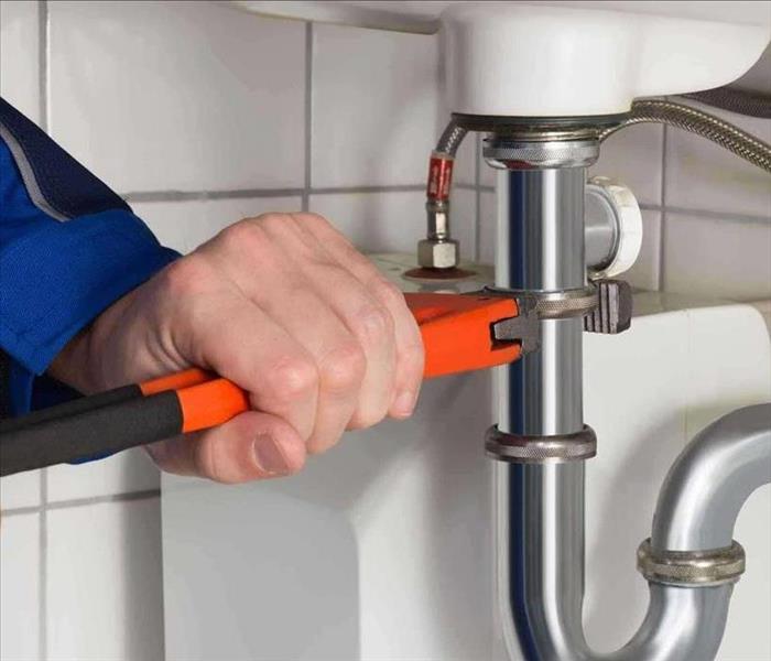 Image of a man holding a wrench trying to tighten an under sink pipe fitting.